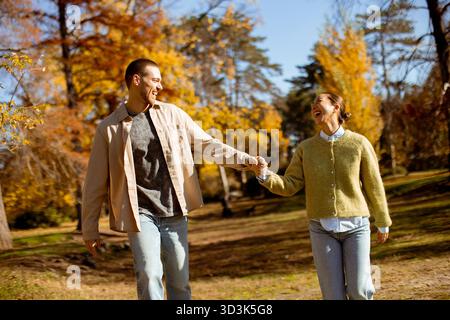 Una coppia felice cammina mano nella mano attraverso un vivace parco pieno di foglie autunnali. Condividono i sorrisi nella calda luce del sole. Foto Stock