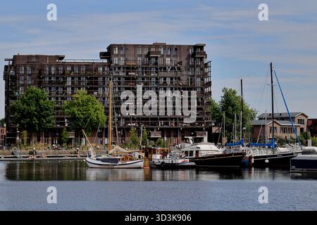 Appartamenti fronte mare a Borneokade, Amsterdam, Paesi Bassi, con alberi a vela e barche da diporto ormeggiate di fronte, visti attraverso le calme acque del canale. Foto Stock