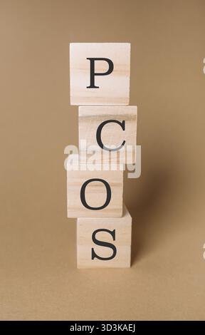 Una pila di blocchi di legno disposti verticalmente su uno sfondo marrone liscio forma la parola PCOS, creando un'esposizione didattica visiva per aumentare la consapevolezza Foto Stock