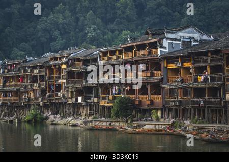 Feng Huang, Cina - agosto 2019 : antiche case storiche in legno e barche turistiche ormeggiate sulla riva del fiume tuo, che scorrono attraverso il centro Foto Stock