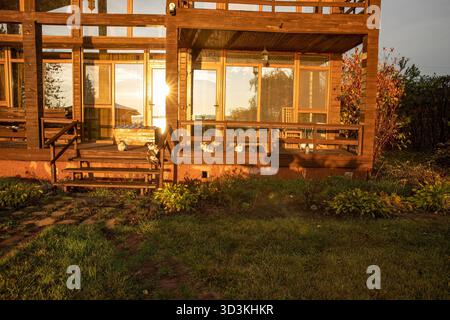 Moderna casa in legno a due piani con grandi finestre illuminate dalla calda luce del tramonto Foto Stock