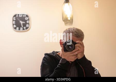 Uomo che fa un autoritratto allo specchio con una fotocamera digitale Foto Stock