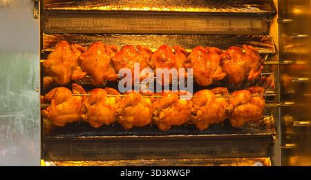 I polli arrostiti sono esposti su uno spiedo rotante in una cucina commerciale, mostrando una pelle dorata e un aspetto appetitoso. Foto Stock
