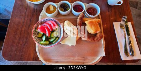 . Colazione variopinta con frutta fresca, pane e vari salse disposti su un piatto di legno, per creare un invitante pasto mattutino Foto Stock