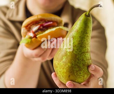 Le mani della donna tengono sia una pera verde fresca che un succoso hamburger, un concetto di scelta alimentare sano e malsano Foto Stock