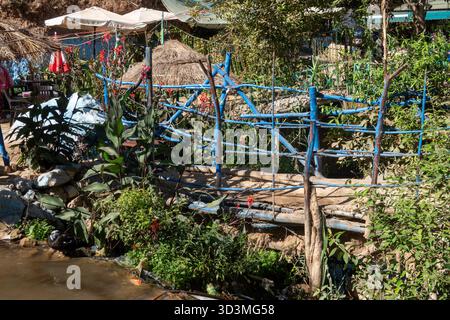 Akchour, Marocco. Una scena rustica e vibrante caratterizzata da un ponte di legno intemprato dipinto di blu brillante, su un piccolo ruscello adagiato tra lussureggianti fogliame. Tratteggio Foto Stock