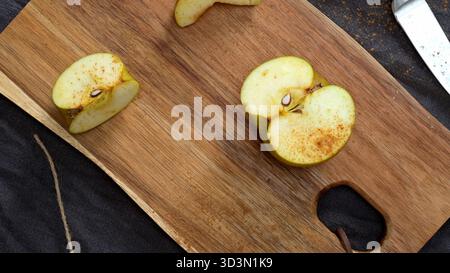 Tre mele dorate si trovano su un rustico tavolo di legno con un panno grigio e un coltello nelle vicinanze, creando un'accogliente scena autunnale. Un tagliere con un'applicazione a fette Foto Stock