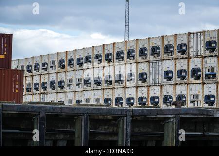Porto di Tauranga, nuova Zelanda. Numerosi contenitori di spedizione refrigerati bianchi impilati in alto nel porto, con una struttura di molo scura in primo piano. Foto Stock