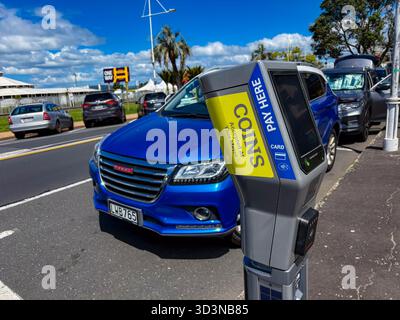 Un moderno parchimetro grigio, che accetta monete e carte, si erge in primo piano con auto parcheggiate visibili in una strada di Tauranga, nuova Zea Foto Stock