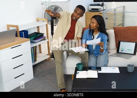 Collaborazione con colleghi afroamericani che analizzano grafici su divano in ufficio, con grafici e tablet Foto Stock