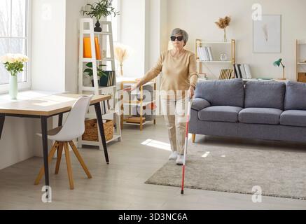 Anziani anziani non vedenti disabili in abiti casual con canna che cammina nel soggiorno di casa. Foto Stock