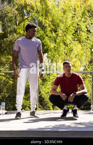 Riposa diversi amici maschi su un ponte di legno vicino alla ringhiera, con una bottiglia d'acqua e orologi da fitness Foto Stock