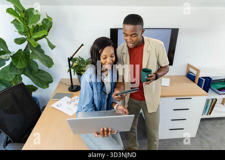 Collaborazione con colleghi afroamericani che analizzano le carte in ufficio, con computer portatile e tazza da caffè Foto Stock