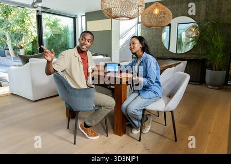 Discutendo della pianificazione di una coppia afroamericana al tavolo da pranzo, con tablet e luci a sospensione Foto Stock
