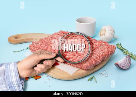Lente d'ingrandimento con abbreviazione di ANALISI DEI RISCHI E PUNTI CRITICI e carne macinata cruda su sfondo azzurro Foto Stock