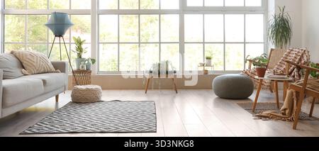 Interno di un luminoso soggiorno con poltrone in legno, divano grigio e piante Foto Stock