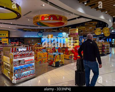 Area commerciale duty-free dell'aeroporto di Auckland con spuntini e cioccolatini, con un uomo che cammina con un bagaglio a mano. Foto Stock