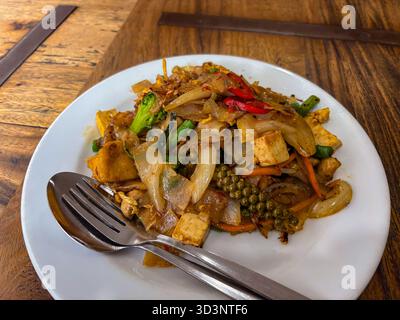 Spaghetti saltati tailandesi speziati. Spaghetti di riso, tofu, broccoli, fagioli verdi, carote, e il peperoncino rosso sono mescolati con un caratteristico coro verde fresco Foto Stock