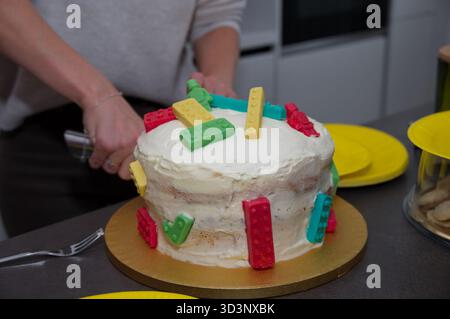 Primo piano della torta di compleanno dei bambini. Le mani delle donne lo tagliano Foto Stock