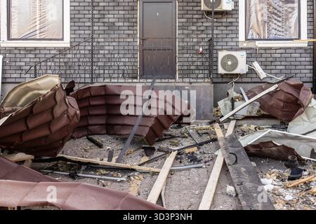 Vista da terra dei danni strutturali dei tetti collassati e dei detriti sparsi davanti alla facciata in mattoni scuri con porte e unità CA, documentando l'impatto Foto Stock