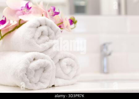 Gli asciugamani sono ordinati con orchidee viola in un bagno luminoso e pulito Foto Stock