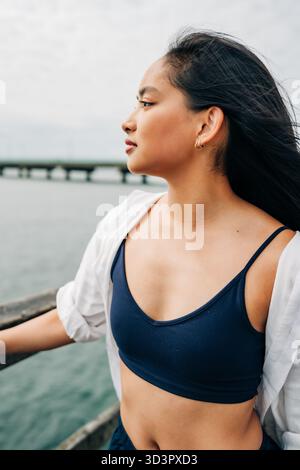 Giovane donna asiatica premurosa che contempla l'oceano sul molo Foto Stock