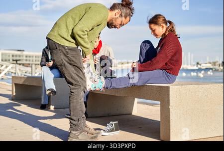 In una bella giornata di sole sul lungomare, una famiglia si riunisce per godersi del tempo di qualità insieme. Un membro sta aiutando un'altra cravatta mentre altri lo fanno Foto Stock