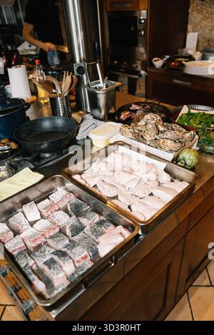 Una varietà di piatti di pesce fresco, tra cui pesce, ostriche e verdure disposte su un bancone della cucina, creando un'atmosfera vivace per gli amanti della cucina Foto Stock