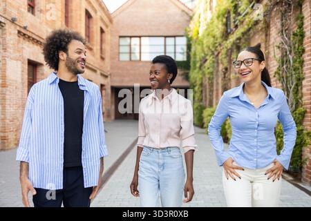 Un team aziendale eterogeneo impegnato in una conversazione vivace mentre cammina attraverso un'area urbana, mettendo in evidenza la collaborazione e il lavoro di squadra in una città vivace Foto Stock