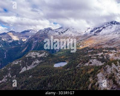 Splendida vista aerea delle Alpi austriache con cime innevate, foreste lussureggianti e un tranquillo lago alpino sotto un cielo parzialmente nuvoloso Foto Stock
