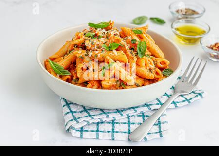 Penne con salsa di pomodoro, condite con foglie di basilico fresco Foto Stock