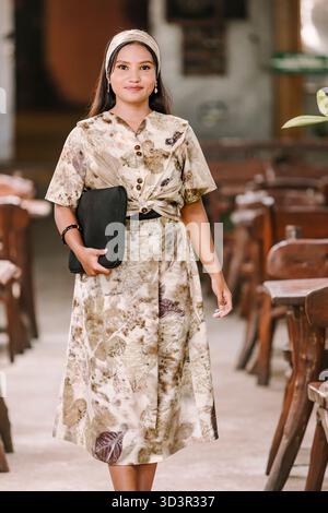 Una donna musulmana modella con fiducia un abito eco-stampato realizzato con tinture naturali, evidenziando la dedizione del sud-est asiatico alla moda sostenibile e al cultu Foto Stock