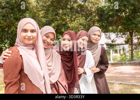 Un gruppo di giovani donne musulmane, che indossano hijab, si gode una giornata di sole all'aperto. Sono amici della generazione Z che stanno ridendo e posando, mostrando il loro Foto Stock