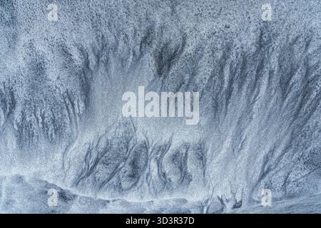 Un'immagine astratta che cattura gli intricati motivi formati da sabbia grigia fine su una spiaggia. Le texture naturali creano un effetto visivo ipnotico Foto Stock