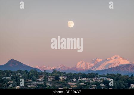 Una vista mozzafiato della luna piena che si innalza sulle montagne di le Mole e del Monte bianco al tramonto, come si vede dalle rive del Lago di Ginevra in Svizzera. Lo scen Foto Stock