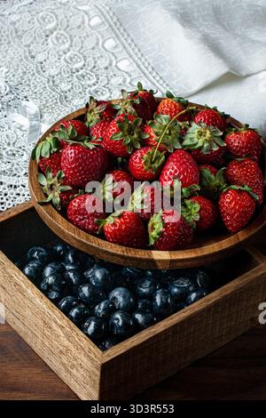 Le fragole e i mirtilli appena raccolti sono splendidamente disposti in ciotole di legno, evidenziandone i colori e le consistenze. Perfetto per una guarigione Foto Stock
