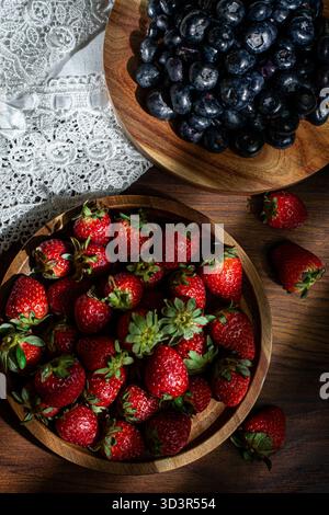 Le fragole fresche e i mirtilli sono disposti artisticamente su piatti di legno. I colori vivaci e le texture rustiche in legno creano un'atmosfera invitante Foto Stock