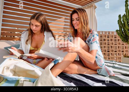 Una madre e una figlia si rilassano insieme in un hotel, godendosi una giornata di sole. Sono seduti su una coperta a strisce, leggono e trascorrono tempo di qualità in pe Foto Stock