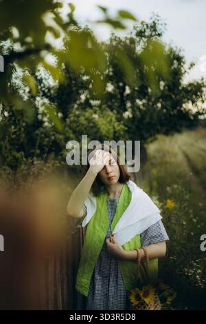 Una donna si staglia con cura in un campo di girasole, indossando un outfit casual con un ukulele in mano. La scena è piena di colori vivaci dell'summe Foto Stock