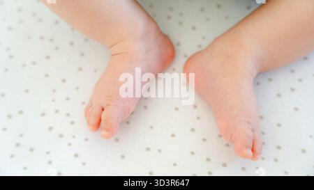 Primo piano degli adorabili piedi di un bambino di tre mesi su una morbida coperta punteggiata. L'immagine cattura l'innocenza e il fascino gentile della prima genitorialità Foto Stock
