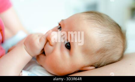 Un delizioso bimbo di 3 mesi succhia tranquillamente il pollice mentre è nascosto tra le braccia di un genitore. L'immagine cattura l'essenza della genitorialità e dell'inno Foto Stock