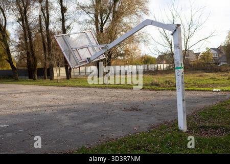 Un canestro da basket rotto e sfalsato si erge su un campo sportivo all'aperto Foto Stock