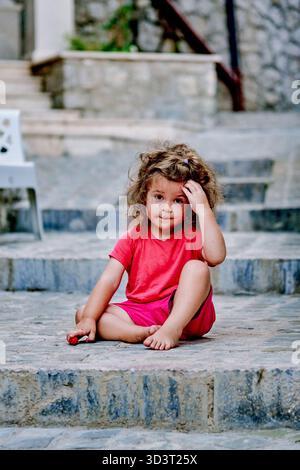 Piccola e premurosa bambina bambina bambina che siede sulle scale fuori dall'infanzia ritratto Foto Stock