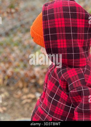 Bambino in giacca a quadri rossa e cappello in maglia arancione all'aperto in autunno Foto Stock