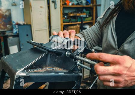 Le mani maschio stringono le parti metalliche insieme al morsetto. Il morsetto è dotato di una vite filettata per il serraggio e la regolazione della pressione. Informazioni generali sulle officine industriali. Foto Stock