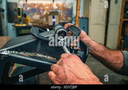 Le mani maschio stringono le parti metalliche insieme al morsetto. Il morsetto è dotato di una vite filettata per il serraggio e la regolazione della pressione. Informazioni generali sulle officine industriali. Foto Stock