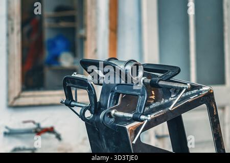 Il morsetto metallico tiene insieme le parti in ferro. Il morsetto è dotato di una vite filettata per il serraggio e la regolazione della pressione. Informazioni generali sulle officine industriali. Foto Stock