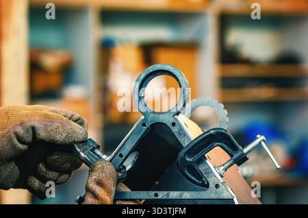 Le mani maschio stringono le parti metalliche insieme al morsetto. Il morsetto è dotato di una vite filettata per il serraggio e la regolazione della pressione. Informazioni generali sulle officine industriali. Foto Stock