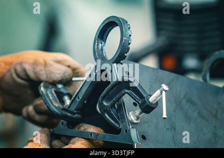 Le mani maschio stringono le parti metalliche insieme al morsetto. Il morsetto è dotato di una vite filettata per il serraggio e la regolazione della pressione. Informazioni generali sulle officine industriali. Foto Stock