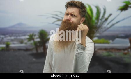 Il lungo barbuto stringe pugno e grida nel verde del parco con palme; sfida lotta frustrazione rabbia. Foto Stock